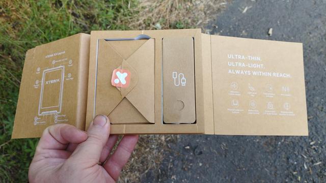 La boîte ouverte ressemble à une sorte de triptique et la partie centrale possède 2 emplacements et chacun contient un emballage plus petit, l'un ressemble à une enveloppe fermée avec son cachet et l'autre bien plus étroit a un dessin représentant un câble usb. Je tiens la chose en main